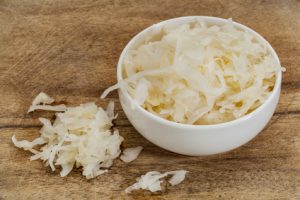 white bowl of sauerkraut on wooden cutting board